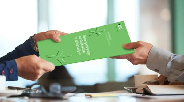 Twee personen geven elkaar een groene publicatie van het AKC aan een bureau.